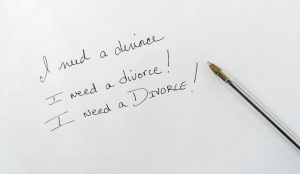A piece of paper with a pen and the words I need a divorce written three times.