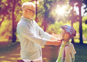 grandfather helping boy with bike helmet at summer park